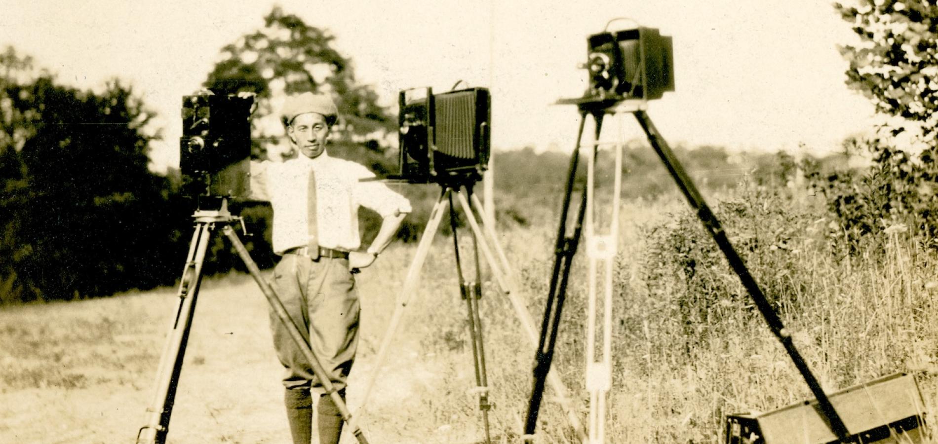 Photographer George Masa stands with two view cameras and a motion-picture camera on the grounds of the Biltmore Estate circa 1920s. Photo courtesy of Buncombe County Special Collections, Pack Memorial Public Library, Asheville, NC.