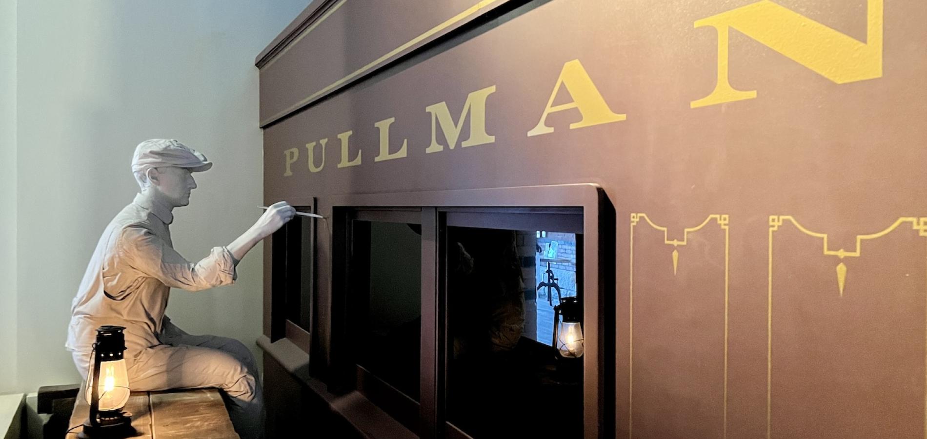 In the Pullman National Historical Park visitor center, a display shows a man hand painting a wooden Pullman railroad car.