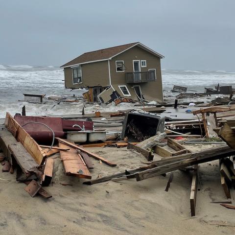 A collapsed house falling into the Atlantic Ocean, surrounded by marine debris. NPS Photo 5-10-2022.