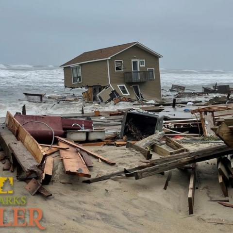 A collapsed house falling into the Atlantic Ocean, surrounded by marine debris. NPS Photo on 5-10-2022.