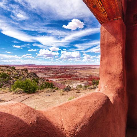 A view of the Painted Desert with a blue sky and white clouds seen through a window frame at the Painted Desert Inn, Petrified Forest National Park