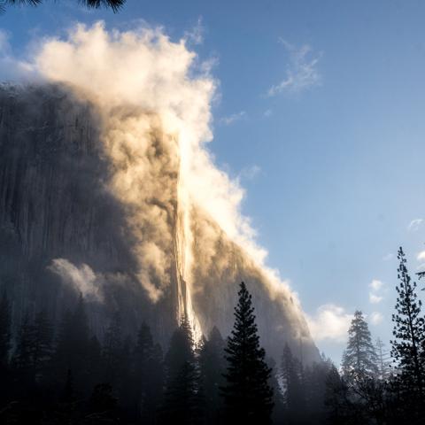 Morning clouds and fog streaming up El Capitan with the sun shining on the cliff face in Yosemite National Park in California