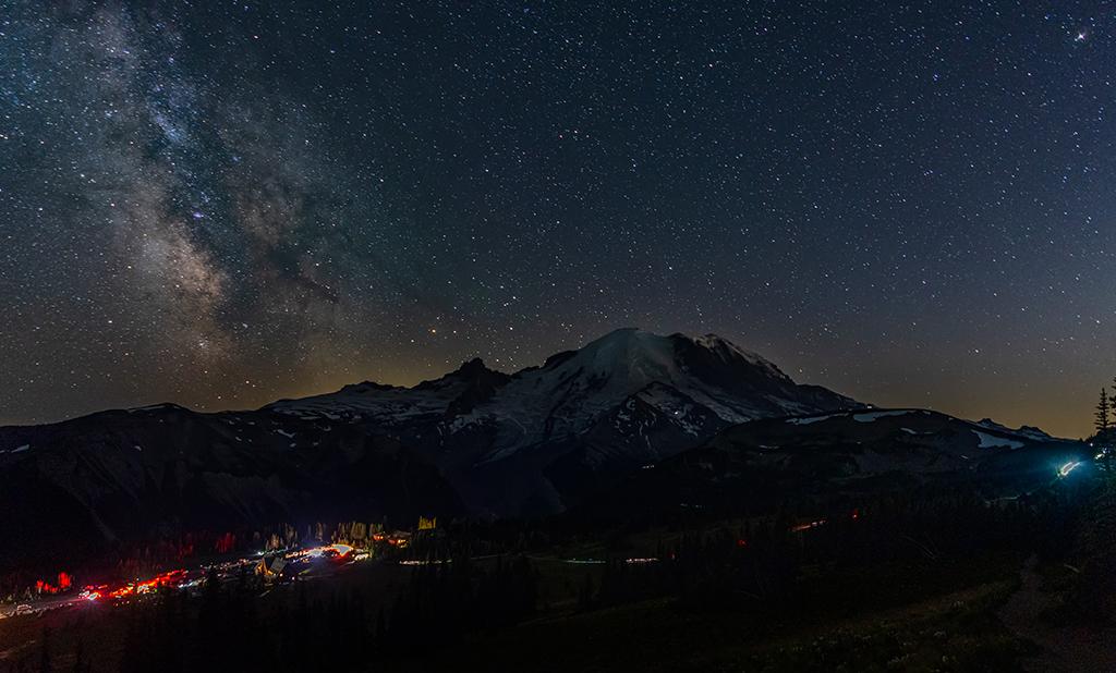 Mount Rainier at night, with stars and the Milky Way in view and a very busy parking lot with people on the trails, Mount Rainier National Park