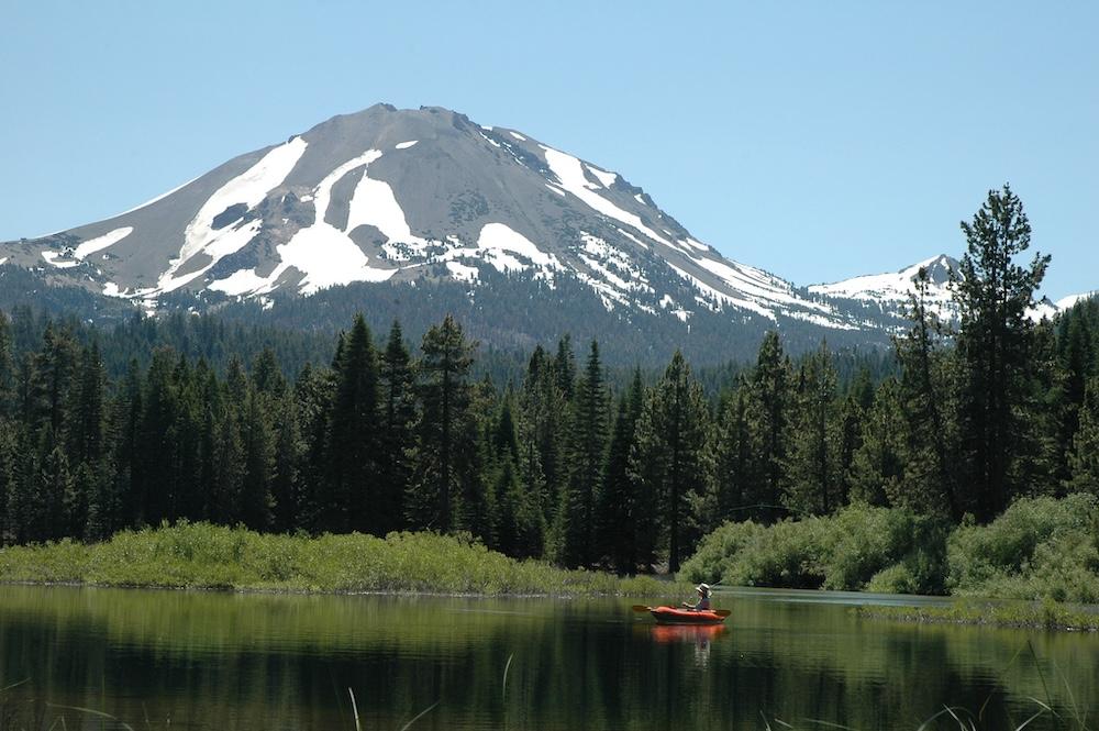 A snow-covered volcano with a person fishing in a lake in the foreground.