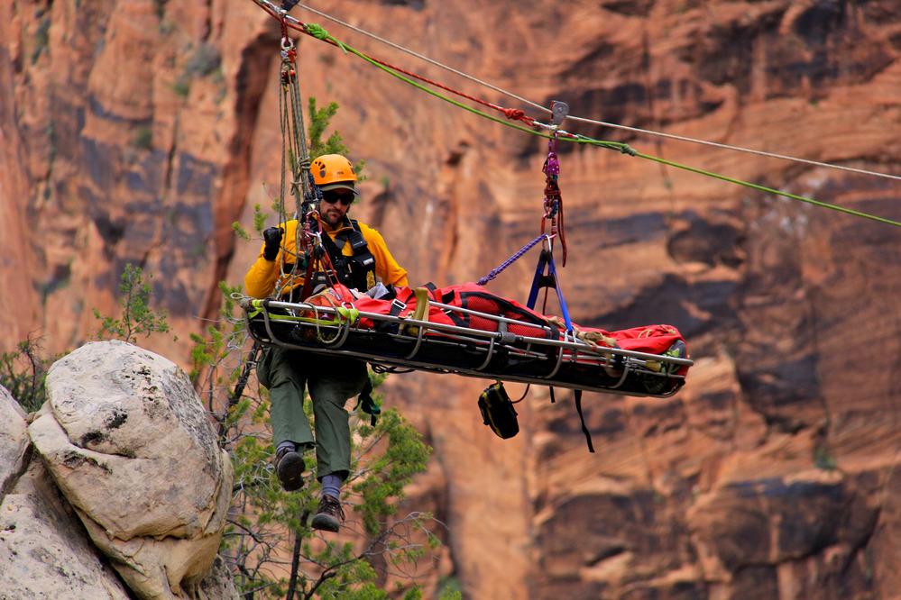 An attendant ranger and simulated patient on a high-line rope with red rocks behind them.