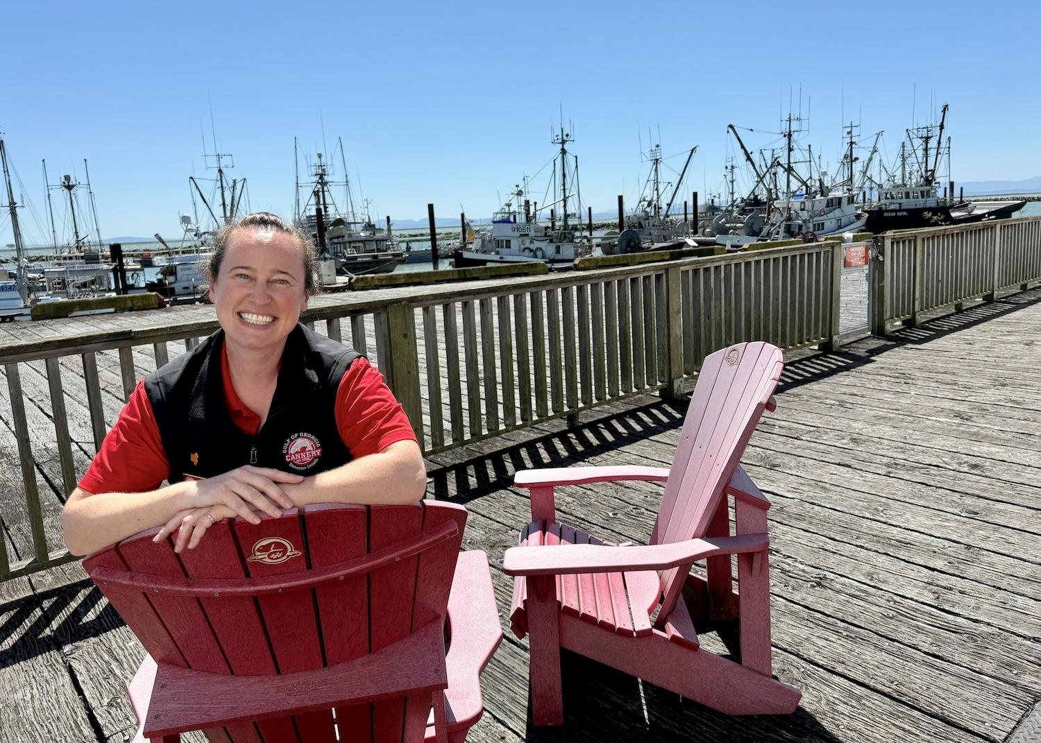 Gulf of Georgia Cannery's head interpreter Jamie Lee sits on Parks Canada chairs on a dock with views of Steveston's working fishing harbor.