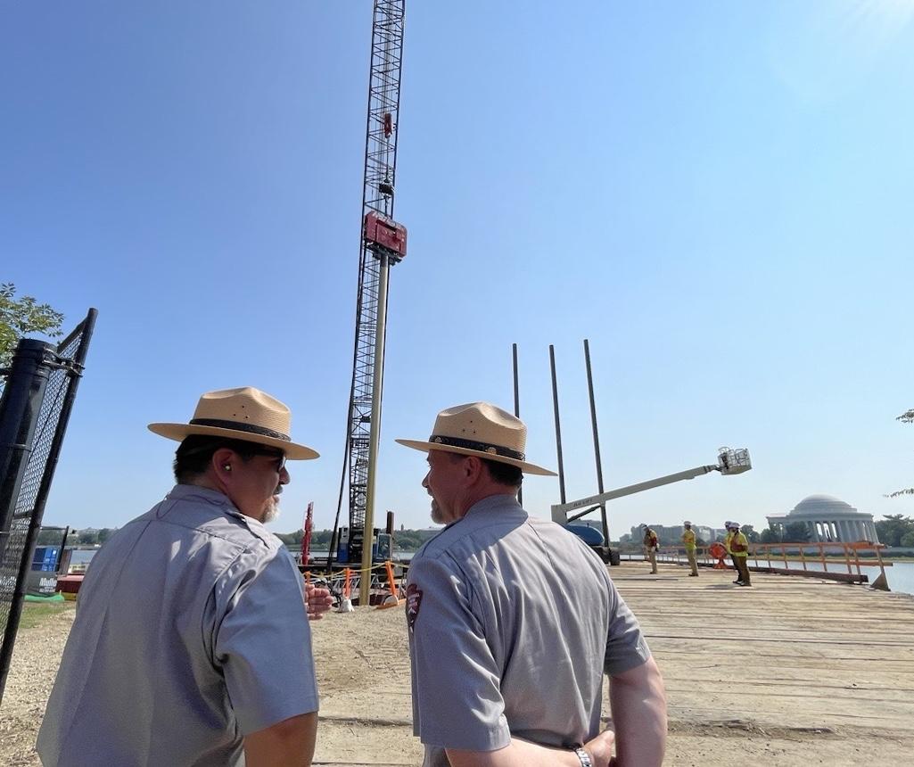 National Park Seeinrvice Director Chuck Sams and National Mall and Memorial Parks Superintendent Jeff Reinbold observe the driving of the first 88-foot-long piling of the Tidal Basin seawall restoration project, funded by the Great American Outdoors Act. 