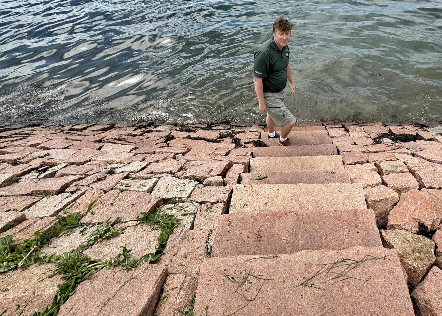 Parks Canada's Kurt Peacock stands by the sea by a wall that's meant to combat coastal erosion.